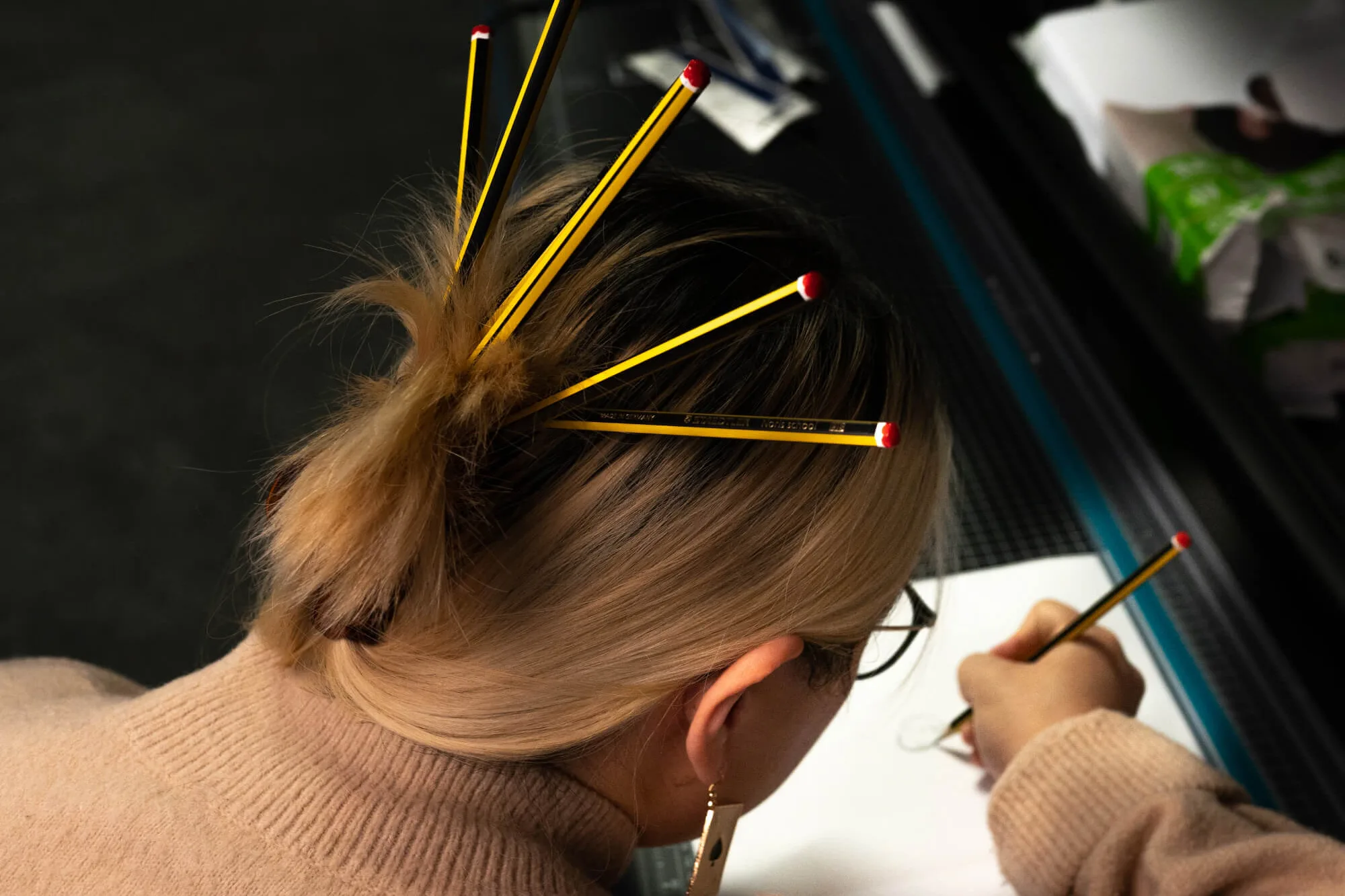 Woman with pencils in her hair drawing on a piece of paper