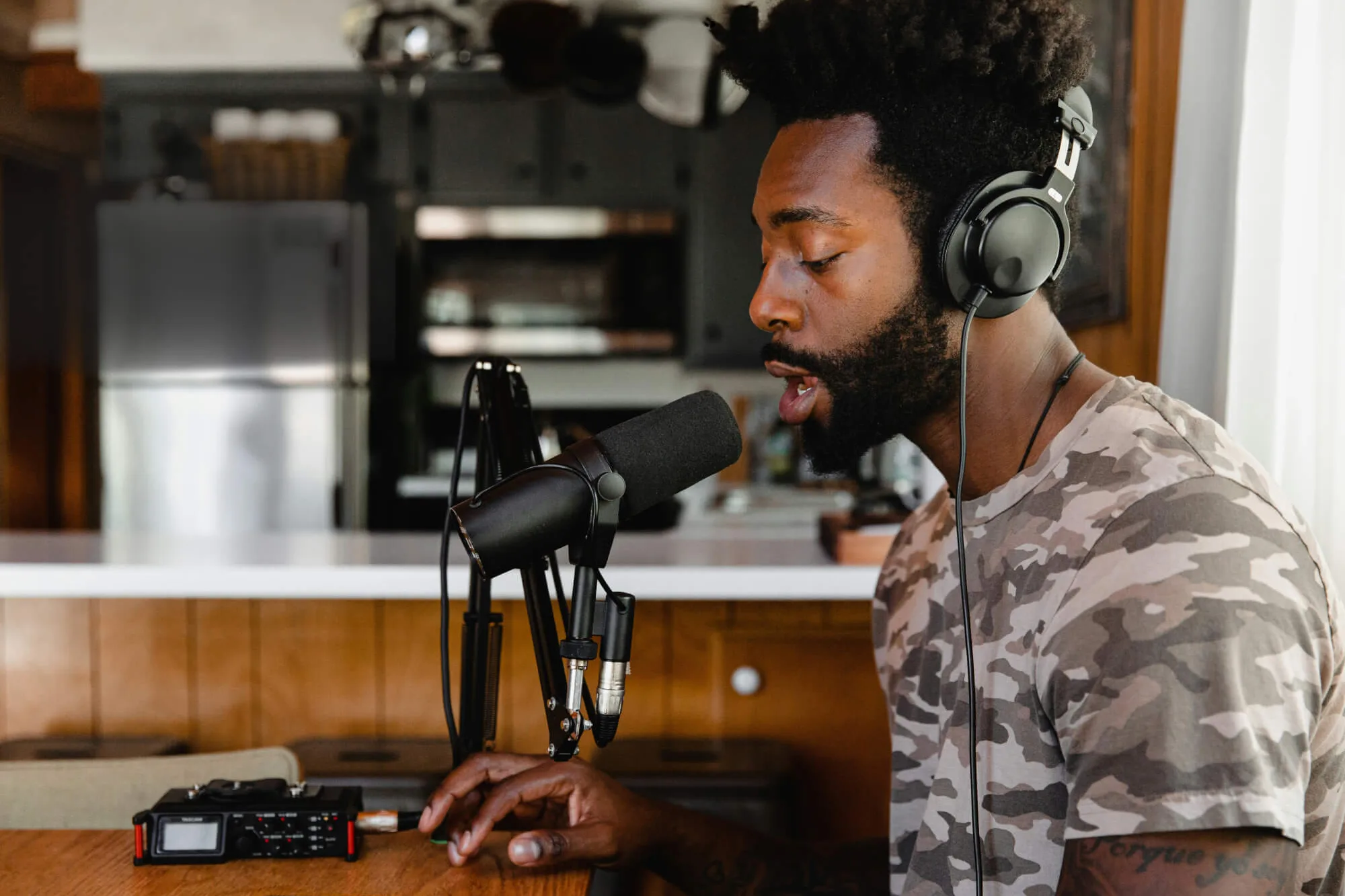 A man working in music or podcasting studio speaking into a microphone whilst looking at his phone.
