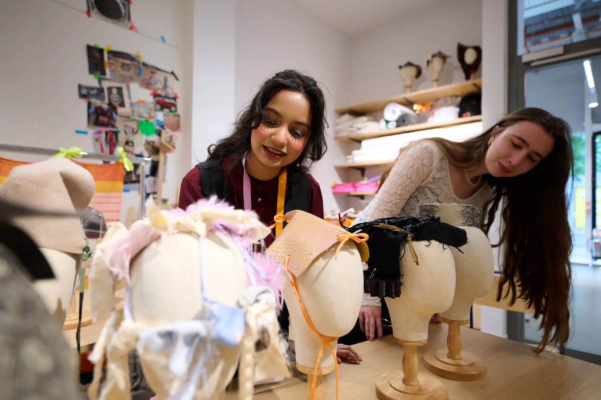 Two young women working with textiles looking at head dress designs on mannequin heads.