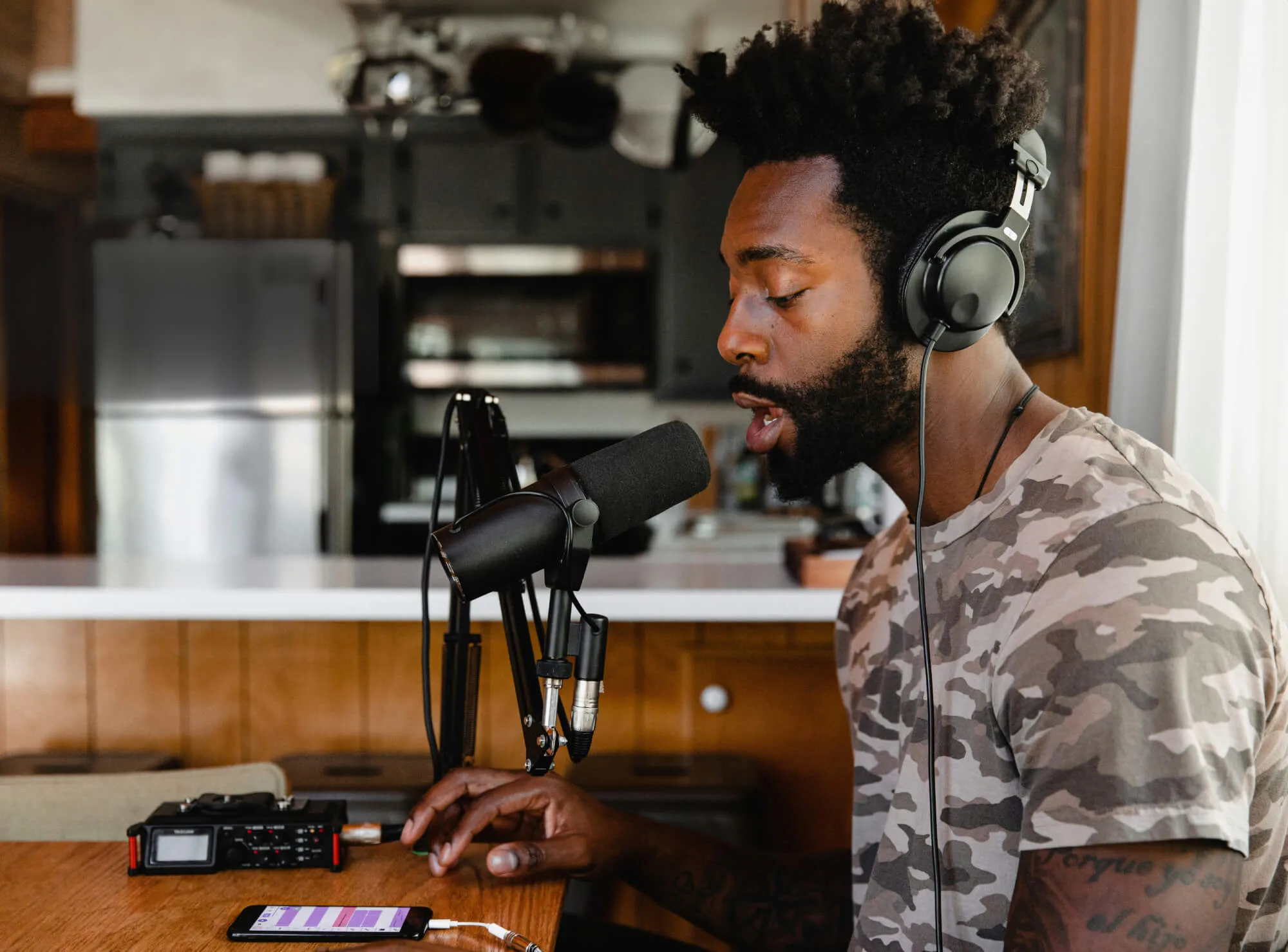 A man working in music or podcasting studio speaking into a microphone whilst looking at his phone.