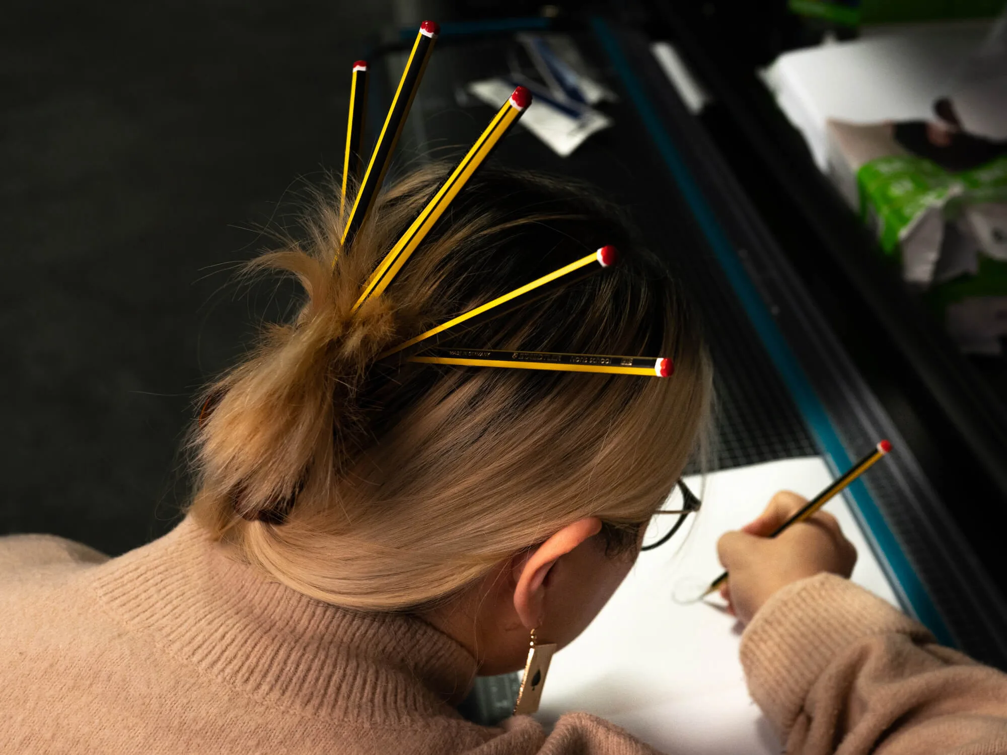 Woman with pencils in her hair drawing on a piece of paper