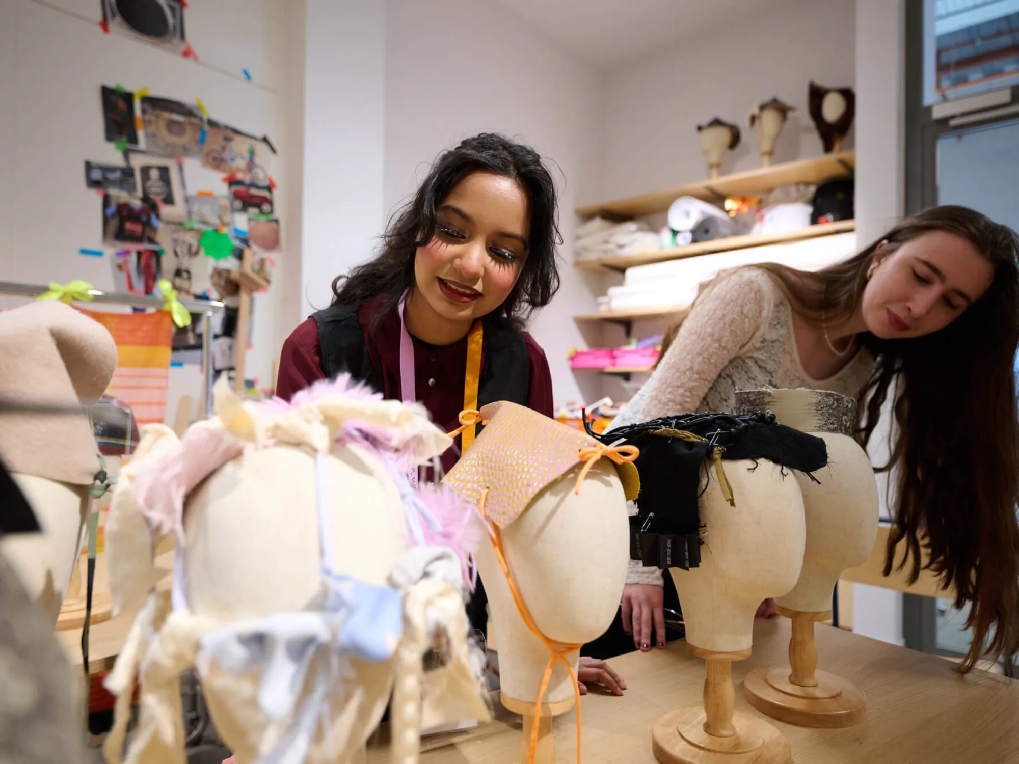 Two young women working with textiles looking at head dress designs on mannequin heads.